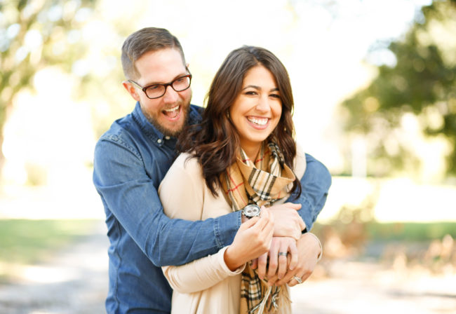 Man hugging woman from behind. Both are smiling but this is a stock photo so it's likely she's weirded out.