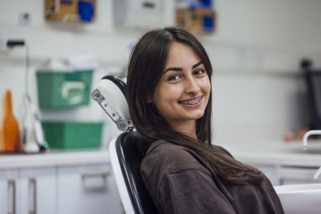 Teenage girl at a dentist practise in Raleigh, NC. She is sitting in a dentists chair smiling, showing the braces on her teeth.