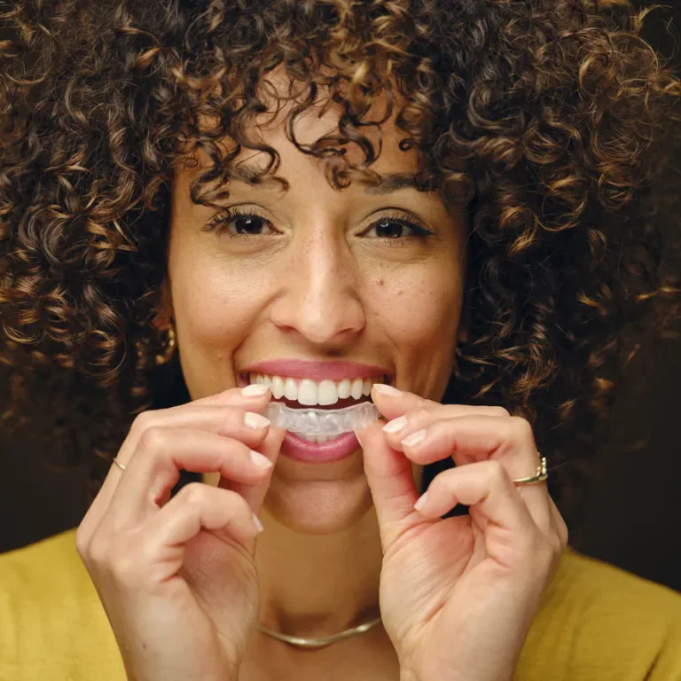 A happy young woman holding invisible clear teeth aligners.